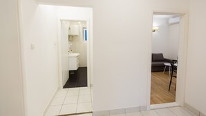 Un pasillo que conduce a un baño con lavamanos y espejo, y una sala de estar con sofá y una mesita.