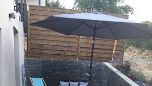 Une terrasse extérieure avec une table et des chaises, une chaise pliante bleue, un mur en pierre et un parasol.
