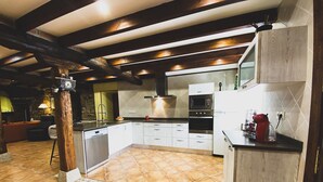 Una cocina con lavavajillas, horno y microondas. Tiene techo de vigas de madera y suelo de baldosas.