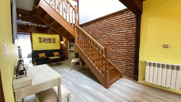 A staircase with wooden balusters leading to an upper floor, a brick wall, a yellow wall, a radiator, a sofa with cushions, and a table with a chair. - La Casa del Pendo (Camargo)