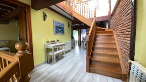 Una escalera con barandilla de madera que conduce a un segundo piso, un comedor con mesa y sillas, y un cuadro en la pared.