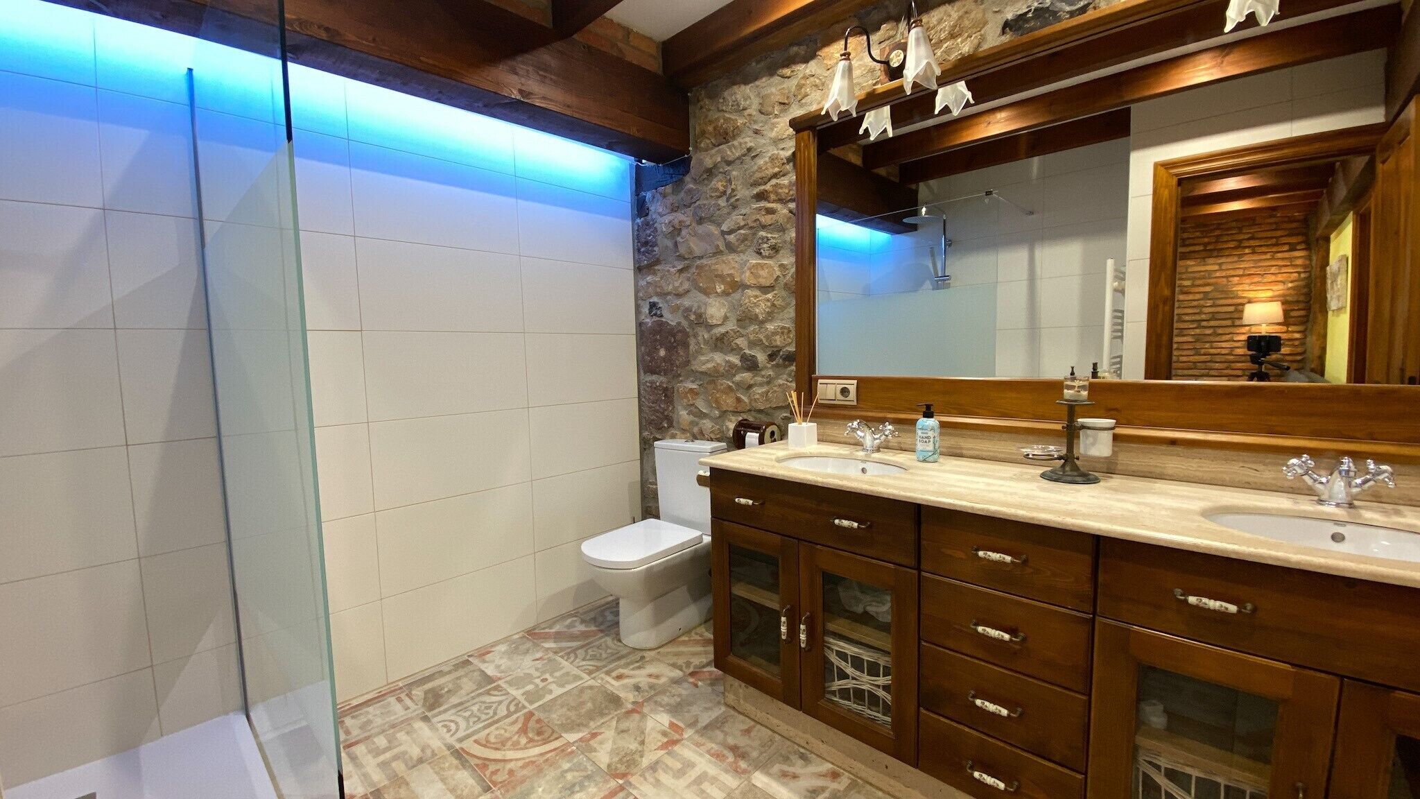 A modern bathroom with a stone accent wall, a large mirror, and a wooden vanity with multiple drawers.