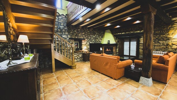 Una sala de estar acogedora con una chimenea de piedra, un televisor y una escalera que sube a un nivel superior.