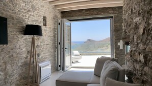 A modern room with stone walls, a large window, a sofa, and a floor lamp. - The Suite by Heliades Villas – Idyllic Getaway in Andros, pool, 2-bedrooms (Cyclades)