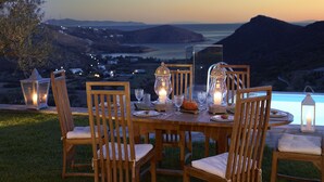 An outdoor dining table set with chairs, candles, and lanterns, overlooking a scenic landscape with mountains and a body of water. - The Suite by Heliades Villas – Idyllic Getaway in Andros, pool, 2-bedrooms (Cyclades)