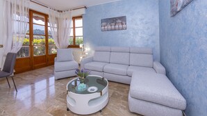 A living room with a grey sofa, a glass coffee table with a vase, a chair, and a view of greenery through a window. - Carlazzo Sant' Agata Apt. 01 (Carlazzo)