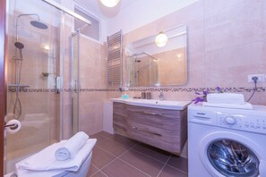 A modern bathroom with a glass shower enclosure, a built-in washing machine, and a vanity with a mirror.