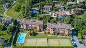 An aerial view of a residential area with multiple two-story houses, a swimming pool, tennis courts, and a parking lot. - Carlazzo Sant' Agata Apt. 01 (Carlazzo)