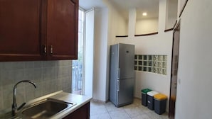 A kitchen with a sink, cabinets, a refrigerator, and trash bins.