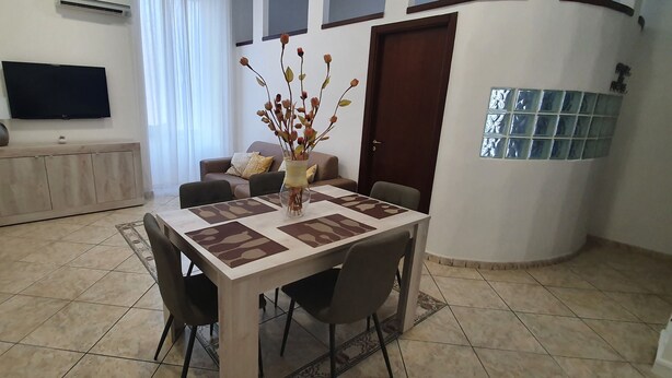 A dining area with a table, chairs, a vase with flowers, a sofa, a TV, and a cabinet.