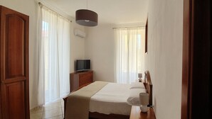 A bedroom with a bed, a TV, a bedside lamp, and a window with curtains.