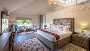 A spacious bedroom with a large bed, a desk, and a chair, featuring a view of the outdoors. - WelcomHeritage Cheetagarh Resort and Spa (Bali)