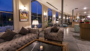 A spacious living area with a large window, a sofa set, a coffee table, and a dining area visible through the window. - WelcomHeritage Cheetagarh Resort and Spa (Bali)