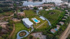 An aerial view of a resort with a swimming pool, multiple buildings, and surrounding natural landscape. - WelcomHeritage Cheetagarh Resort and Spa (Bali)