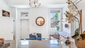 Ein modernes Wohnzimmer mit einer großen Granitabdeckung, einem blauen Sofa, einem runden Spiegel und Blick auf ein Backsteingebäude durch ein Fenster.
