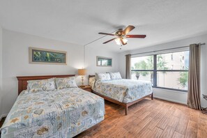 Une chambre avec deux lits, un ventilateur de plafond et une grande fenêtre avec des rideaux.
