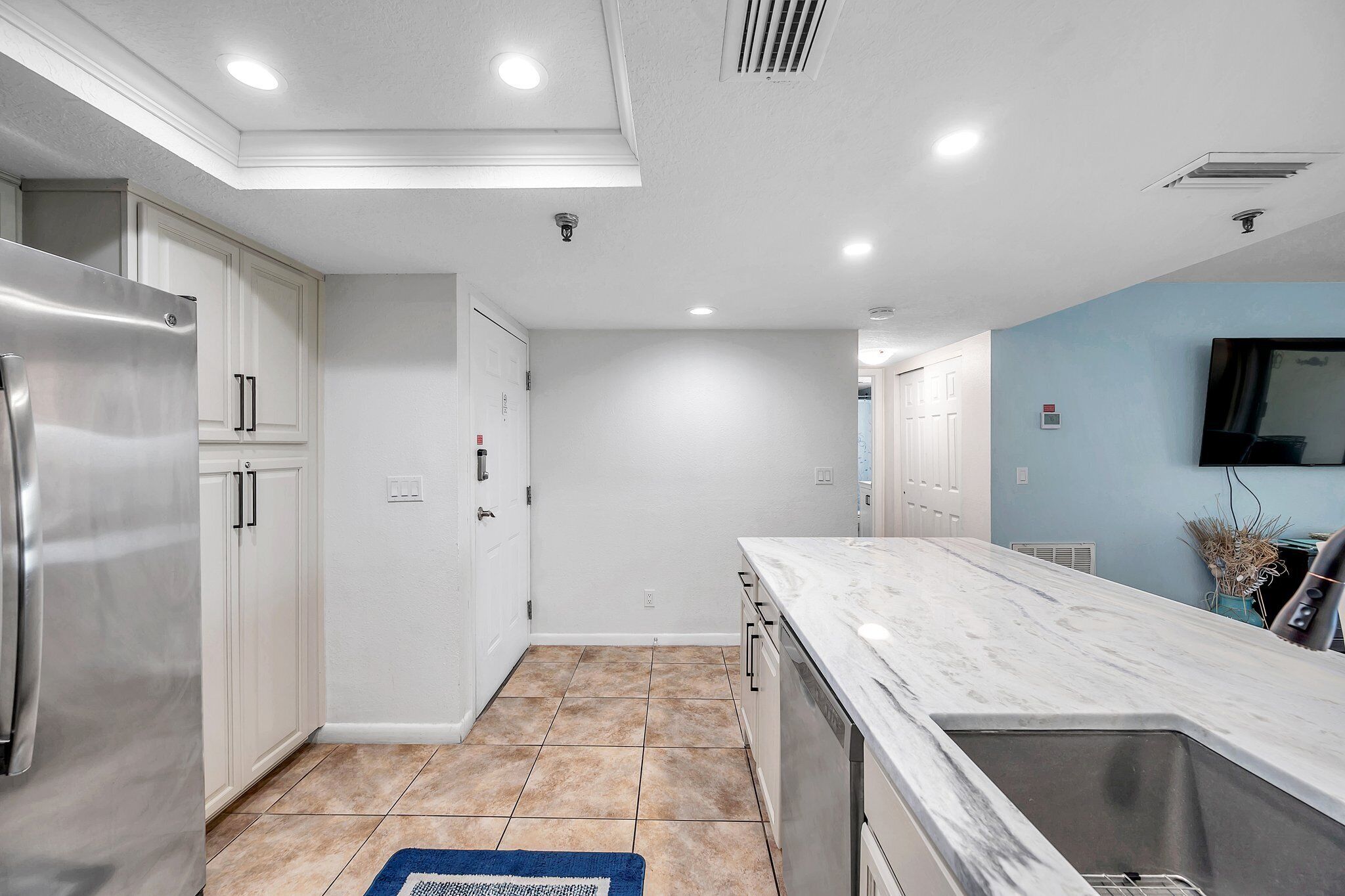 Una cocina moderna con armarios blancos, un refrigerador de acero inoxidable, encimera de mármol y lavavajillas integrado.