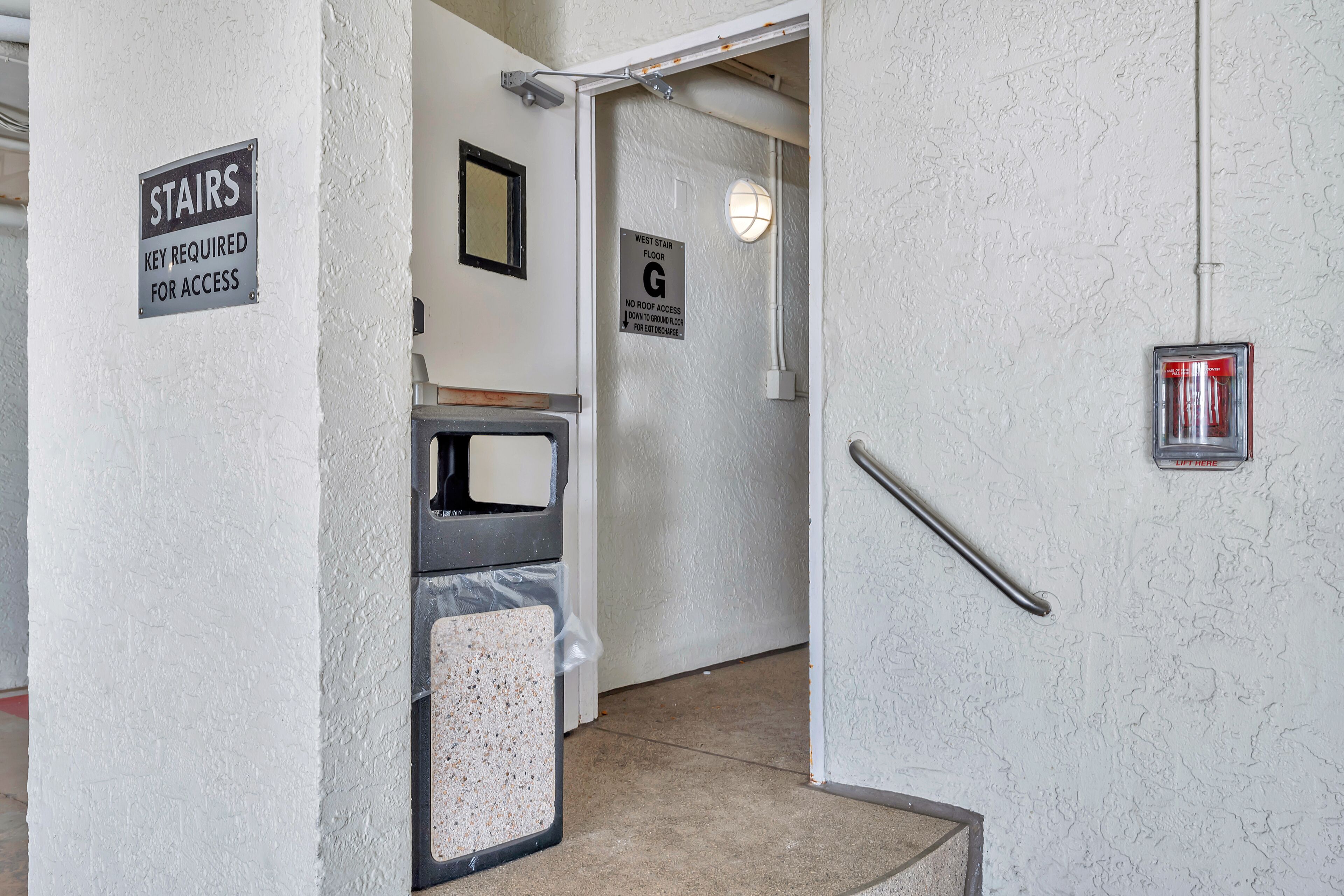 A hallway with a sign indicating 'Stairs Key Required for Access' and another sign for 'West Stair Floor G No Roof Access Down to Ground Floor for Exit Discharge.'