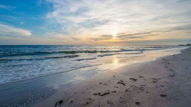 Ein Strand mit Sonnenuntergang, Wellen und Fußabdrücken im Sand.