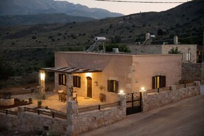 A stone building with a flat roof, outdoor seating area, and a view of mountains in the background.
