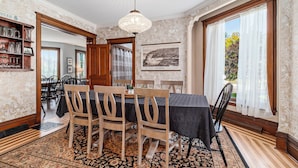 Une salle à manger avec une table dressée pour quatre personnes, des chaises en bois, un lustre et un tapis à motifs.