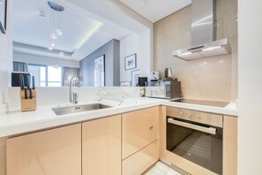 A modern kitchen with a stainless steel sink, a built-in oven, and a microwave. There are wooden cabinets and a white countertop. - Cool Dubai Apt next Burj Khalifa & Design District (Dubai)