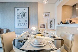 A dining area with a glass table, chairs, and a kitchen in the background.