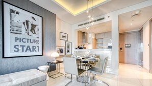A modern living room with a sofa, dining table, and chairs. There is a kitchen area with cabinets and a stove. - Cool Dubai Apt next Burj Khalifa & Design District (Dubai)