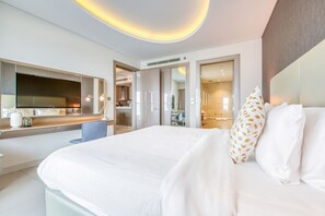 A modern hotel room with a large bed, a flat-screen TV, a desk with a chair, and a bathroom visible through an open door.