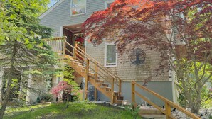 A two-story house with a wooden staircase leading to a balcony. - Cape Cod Villa pond front vacation home, retreat, spa, venue, film location (Harwich - Brewster Border)