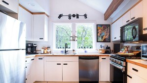 A modern kitchen with white cabinets, a dishwasher, a stove, and a large window with a view of trees. - Cape Cod Villa pond front vacation home, retreat, spa, venue, film location (Harwich - Brewster Border)