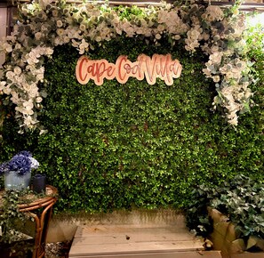 Eine Wand mit weißen Blumen und einem Holzschild mit der Aufschrift 'Cafe de Vida'.