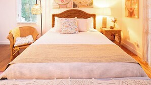 A bedroom with a large bed, a wicker chair, a bedside table with a lamp, and wall art. - Cape Cod Villa pond front vacation home, retreat, spa, venue, film location (Harwich - Brewster Border)