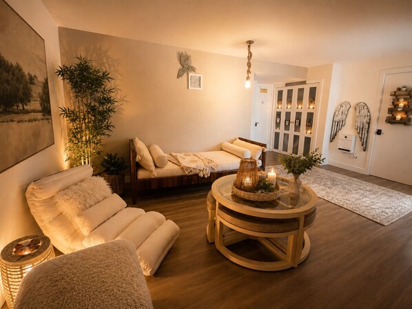 A cozy living room with a sofa, a round wooden coffee table with candles, a large plant, and a wall-mounted decorative piece. - Cape Cod Villa pond front vacation home, retreat, spa, venue, film location (Harwich - Brewster Border)