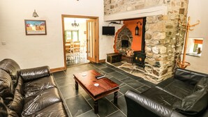 A cozy living room with leather sofas, a stone fireplace, and a dining area visible through an open door. - Trewrach Cottage (Newport)