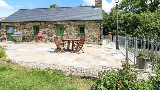 A stone house with a tiled patio, a barbecue, and a fenced garden area. - Trewrach Cottage (Newport)