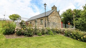 A stone building with a sloped roof, surrounded by a well-maintained garden with various flowering plants. - Trewrach Cottage (Newport)