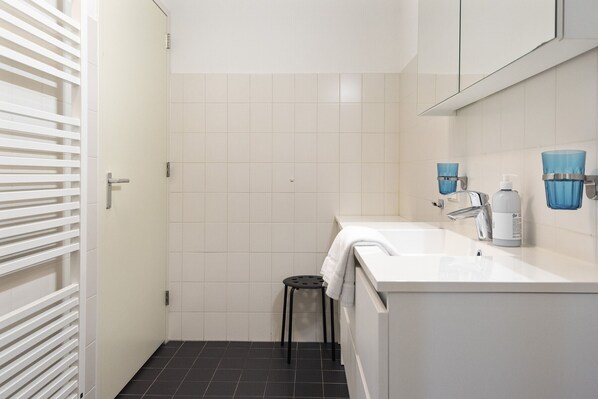 A bathroom with white tiles, a sink, a mirror, and a towel rack. - Spacious and luxurious first flloor apartment with balcony- Kaag (9) (Warmond)