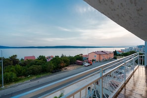 Un balcon donnant sur une route, avec des bâtiments et une étendue d’eau visibles au loin.