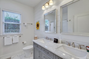A bathroom with a large mirror, two sinks, a toilet, and a window with blinds.