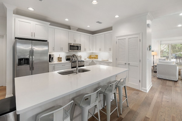 A modern kitchen with white cabinetry, stainless steel appliances, and a central island with bar stools.