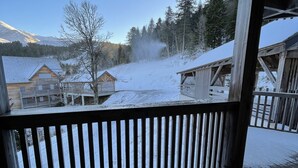 Une véranda en bois offrant une vue sur un village enneigé et sur des montagnes en arrière-plan.
