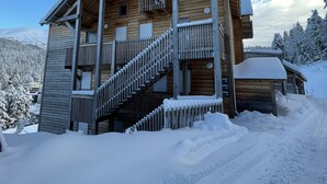 Un chalet en bois doté d’un balcon et d’un escalier, entouré d’arbres couverts de neige et surplombant un ciel dégagé.