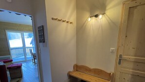 Une pièce comprenant un banc en bois, une petite poubelle, un luminaire fixé au mur et une porte.