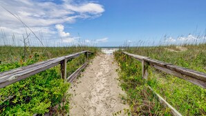 Un sentier de sable bordé de rambardes en bois, qui mène à l’océan.