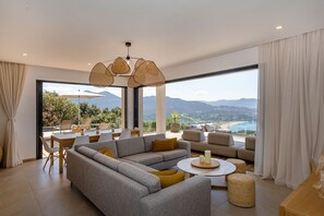 A modern living room with a large sofa, a dining table, and a view of a mountainous landscape.