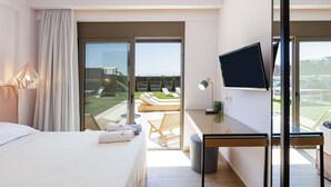 Een hotelkamer met een bed, een bureau met een televisie en een balkon met uitzicht op het omliggende landschap.