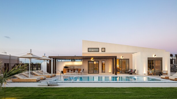 Een modern huis met een zwembad, buitenmeubilair en een goed verlicht terras.