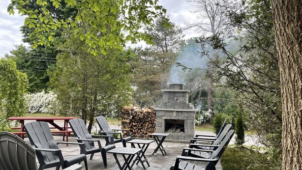 An outdoor patio with Adirondack chairs and a stone fireplace. - Country Suite - Private HotTub, KingBd, Downtown (Wolfville)