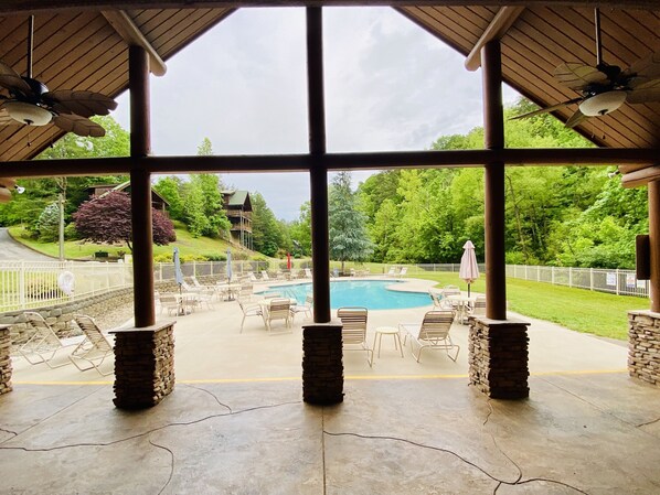 Un espacio exterior techado con piscina, sillas de descanso y vistas a un paisaje verde.